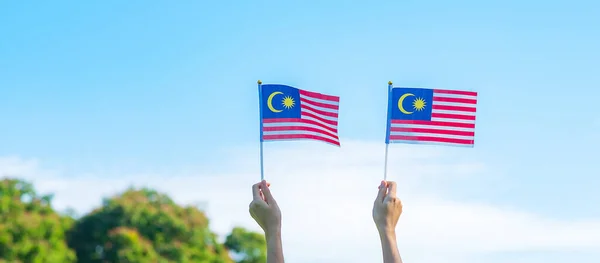 stock image hand holding Malaysia flag on blue sky background. September Malaysia national day and August Independence day