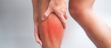 Gri arka planda kas ağrısı olan yetişkin bir erkek. Baldır kası çekilmesi yüzünden bacağı ağrıyan yaşlı bir adam. Spor yaraları ve tıbbi konsept