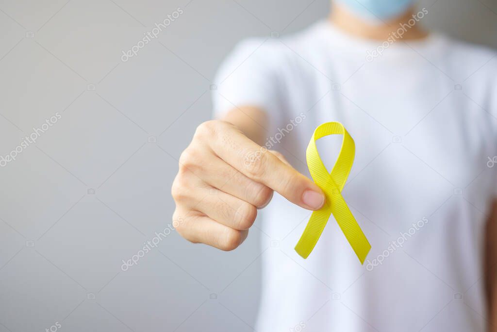 hand holding Yellow Ribbon for supporting people living and illness. September Suicide prevention day, Childhood, Sarcoma and bone cancer awareness month concept