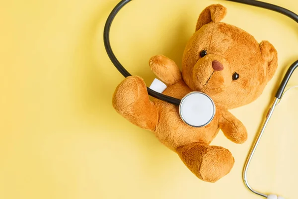 Stethoscope with Bear doll on yellow background for supporting kid living and illness. September Childhood Cancer Awareness month, healthcare and life insurance concept