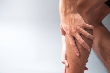 Gri arka planda kas ağrısı olan yetişkin bir erkek. Baldır kası çekilmesi yüzünden bacağı ağrıyan yaşlı bir adam. Spor yaraları ve tıbbi konsept