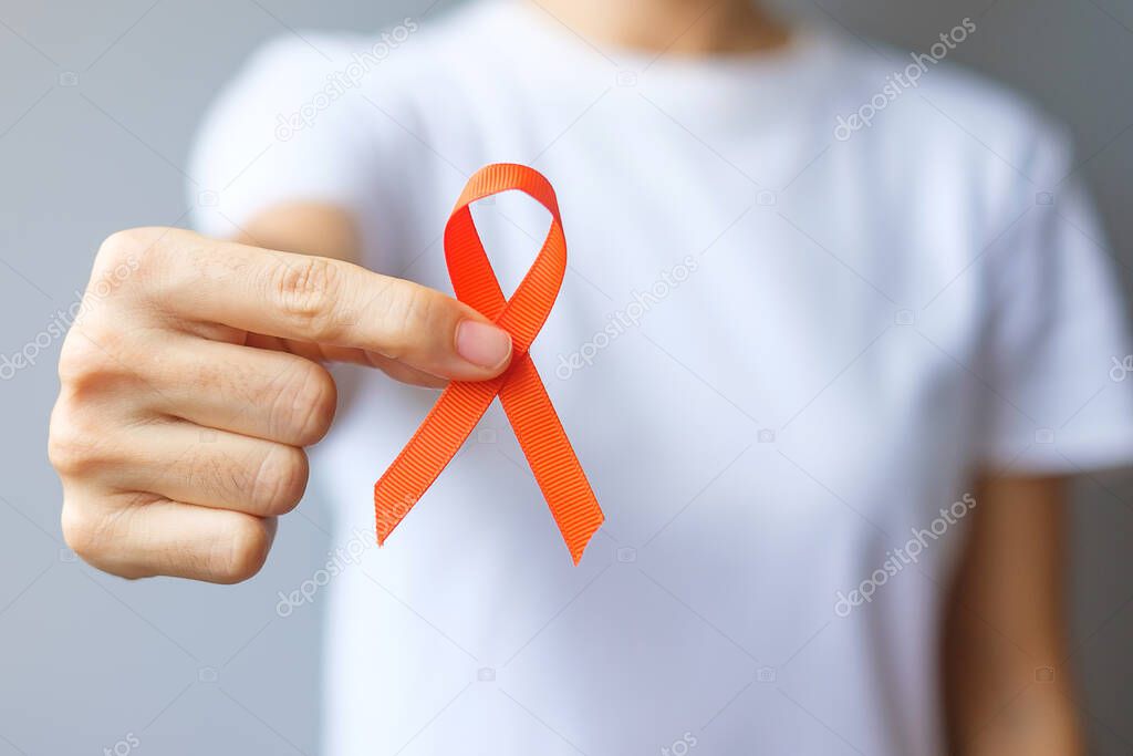 hand holding Orange Ribbon for Leukemia, Kidney cancer day, world Multiple Sclerosis, CRPS, Self Injury Awareness month. Healthcare and word cancer day concept