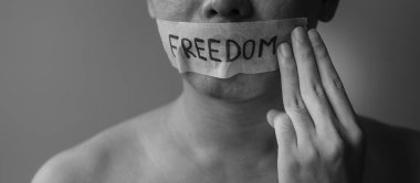 Adam, Özgürlük mesajıyla yapıştırılmış ağzı yapışkan bantlı üç parmak gösteriyor. Konuşma özgürlüğü, İnsan Hakları, Protesto diktatörlüğü, demokrasi, özgürlük, eşitlik ve kardeşlik kavramları