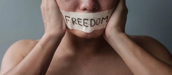 Man with mouth sealed in adhesive tape with Freedom message. Free of speech, freedom of press, Human rights, Protest dictatorship, democracy, liberty, equality and fraternity concepts