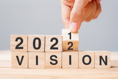 İş adamı ahşap küpü tutuyor ve masa arkasında 2021 nolu bloktan 2022 VISION 'a çeviriyor. Çözüm, plan, amaç, görev, değer ve yeni yıl tatili kavramları