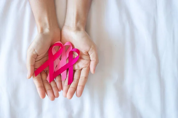 October Breast Cancer Awareness month, adult Woman  hand holding Pink Ribbon on pink background for supporting people living and illness. International Women, Mother and World cancer day concept