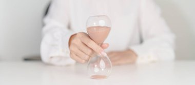 Masa başında kum saati olan kadın kum saatinin geçişini ölçen kum saati ampulünün içinden akıyor. Geri sayım, teslim tarihi, yaşam süresi ve emeklilik kavramı