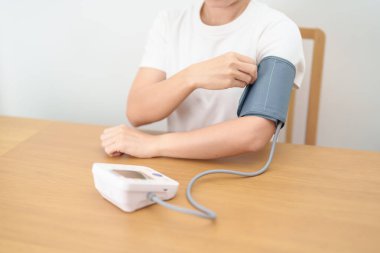 Kan basıncı monitöründen kadın kelepçeyle kan basıncını ölçüyor. Sistolik, SYS, Diyastolik, DIA, Nabız, Hipertansiyon, Hipotansiyon, Kalp hızı, Kardiyovasküler Hastalık ve Mayıs Dünya Hipertansiyon Günü