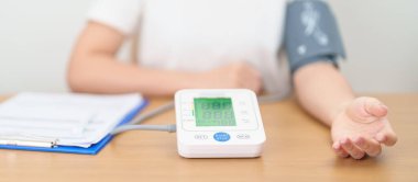 Kan basıncı monitöründen kadın kelepçeyle kan basıncını ölçüyor. Sistolik, SYS, Diyastolik, DIA, Nabız, Hipertansiyon, Hipotansiyon, Kalp hızı, Kardiyovasküler Hastalık ve Mayıs Dünya Hipertansiyon Günü