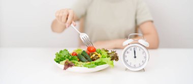 Taze organik sebze tabağı ve çalar saati olan mutlu bir kadın. Aralıklı oruç, eğer, yemek zamanı, beslenme, kilo kaybı, temiz yemek, sağlıklı gıda yeme, sağlıklı beslenme, diyet ve yaşam tarzı