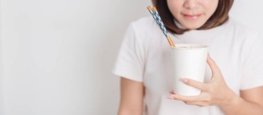 Mutlu genç Asyalı kadın evde dinlenirken lezzetli bir fincan hazır eriştenin tadını çıkarırken neşeli bir kadın dairede gülümseyerek hazır ramen yiyor. Basit yaşam tarzı ve hızlı yemek konsepti