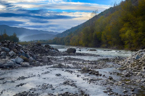 Aydınlatılmış tepeleri olan yüksek dağları olan güzel bir manzara, dağ gölündeki taşlar, yansıma, mavi gökyüzü ve gündoğumunda sarı güneş ışığı.