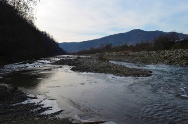 Kış manzarasında donmuş bir nehir. Ormanlı kış manzarası, bulutlu gökyüzü ve güneş.