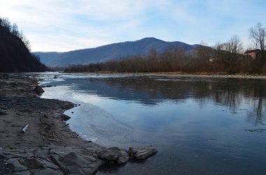 Kış manzarasında donmuş bir nehir. Ormanlı kış manzarası, bulutlu gökyüzü ve güneş.