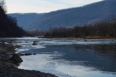 Kış manzarasında donmuş bir nehir. Ormanlı kış manzarası, bulutlu gökyüzü ve güneş.