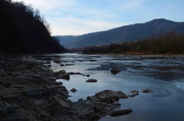 Kış manzarasında donmuş bir nehir. Ormanlı kış manzarası, bulutlu gökyüzü ve güneş.