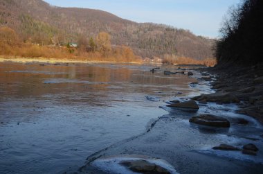 Kış manzarasında donmuş bir nehir. Ormanlı kış manzarası, bulutlu gökyüzü ve güneş.