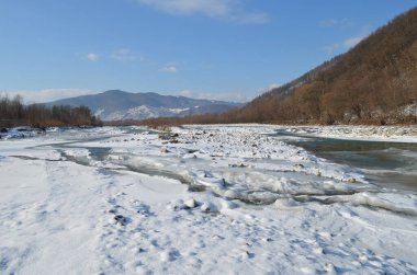 Kış manzarasında donmuş bir nehir. Ormanlı kış manzarası, bulutlu gökyüzü ve güneş.