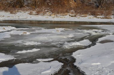 Kış manzarasında donmuş bir nehir. Ormanlı kış manzarası, bulutlu gökyüzü ve güneş.