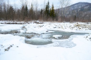 Kış manzarasında donmuş bir nehir. Ormanlı kış manzarası, bulutlu gökyüzü ve güneş.