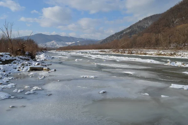 A frozen river in a wintry landscape. Winter landscape with forest, cloudy sky and sun.