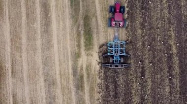 Harrows 'lu kırmızı traktör tarımı hasat için hazırlıyor. Drone hava perspektifi görünümü.