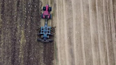 Harrows 'lu kırmızı traktör tarımı hasat için hazırlıyor. Drone hava perspektifi görünümü.