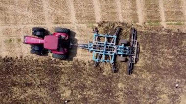 Harrows 'lu kırmızı traktör tarımı hasat için hazırlıyor. Drone hava perspektifi görünümü.