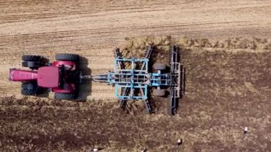 Harrows 'lu kırmızı traktör tarımı hasat için hazırlıyor. Drone hava perspektifi görünümü.