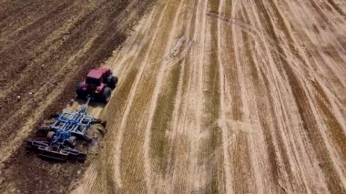 Harrows 'lu kırmızı traktör tarımı hasat için hazırlıyor. Drone hava perspektifi görünümü.