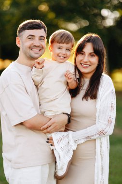 Mutlu genç aile altın saatinde dışarıda poz veriyor, anne babalar parkta kucaklaşırken gülümseyen bebeklerini tutuyorlar; sıcak doğal ışık, günlük kıyafetler, neşeli bağlantı ve ebeveynlik anları.