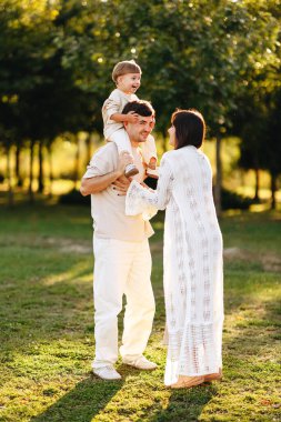 Genç ebeveynler neşeli bir anı paylaşıyorlar. Baba, gülen oğullarını güneşli bir parkta omuzlarında taşırken. Sevgiyi, sıcaklığı, oyunculuğu ve aile bağlarını açık havada kurarken..