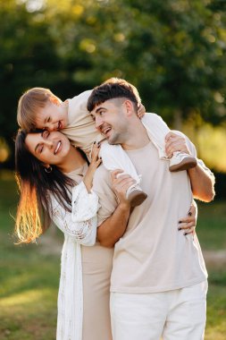 Genç ebeveynler neşeli bir anı paylaşıyorlar gülen çocuklarını güneşli bir parkta babalarının omuzlarında taşıyorlar..