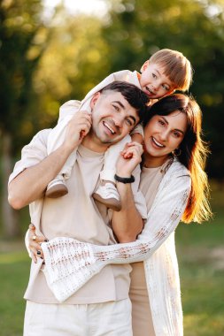 Genç ebeveynler ve küçük oğulları güneşli bir parkta sıcak ve neşeli bir anı paylaşıyorlar. Gülümseyen aile sevgiyi, birlikteliği, oyunculuğu ve rahat hafta sonu yaşam tarzını kucaklıyor..