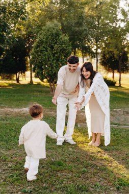 Genç ve mutlu bir aile, altın saat ışığı altında, ebeveynler ve çocuklar arasındaki neşeli bağları, güveni ve açık havada geçen anları yakalayarak, gün ışığı altındaki parkta onlara doğru koşan çocuklarını izler..