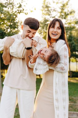 Genç bir çift, güneşli bir parkta gülüp eğlenen çocuklarını kucaklıyor, sıcak aile bağlarını, kaygısız yaz neşesini ve ebeveynleriyle mutlu çocukları arasındaki sevgi dolu anları yakalıyor..