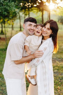 Neşeli genç bir aile, parkta altın saatinde gülen çocuklarını kucaklıyor. Sıcak bir bağ, neşeli ebeveynlik ve yakın aile bağlarını açık havada gösteriyor..