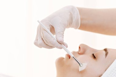 Profesyonel estetisyen, müşterisi rahatlarken, cilt bakımı, güzellik ve sağlıklı, parlayan cilt için temiz bir spa ortamında pohpohlama yaparken, bir yelpaze fırçasıyla nazik bir yüz tedavisi uyguluyor..