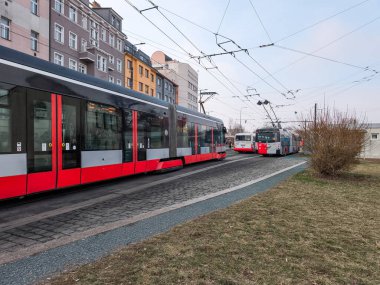 Prag, Çek Cumhuriyeti - 26 Şubat 2025: Zenklova caddesinde bulutlu bir gökyüzü altında tramvayın önünden geçen kırmızı ve gri tramvay, Palmovka Liben ilçe trafik sıkışıklığı altında kentsel ulaşım hayatı
