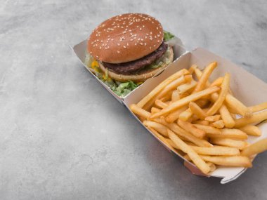 Gri bir arka planda, fast food kutusunda servis edilen susamlı çörek ve patates kızartması ile nefis bir hamburger, klasik fast food galentines gününü temsil ediyor.