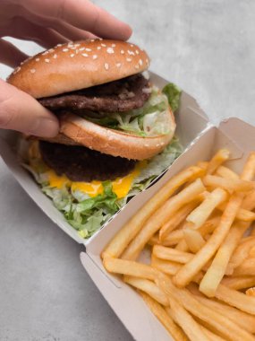 Çift katlı çizburgerin üst topuzunu kaldırırken iki köfte, peynir ve marul, patates kızartmasının yanında servis edilmiş.