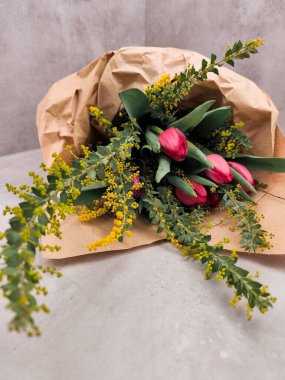 Pembe lale buketi ve kahverengi el işi kağıda sarılı sarı mimoza çiçekleri gri desenli arka plan anneleri gününde dinleniyor.