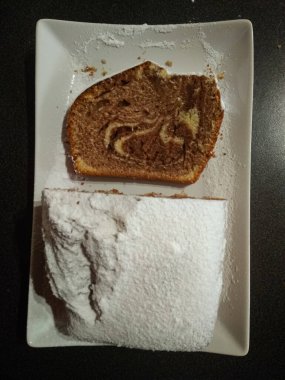 Taze pişmiş mermer kek üzerine krema serpiştirilmiş şeker serpilmiş, beyaz dikdörtgen bir tabakta dinleniyor, tadını çıkarmaya hazır.