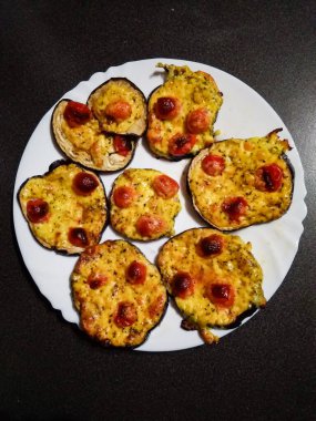 Eritilmiş peynir ve kiraz domatesli ızgara patlıcan dilimleri, özel mini pizzalar, beyaz tabakta servis edilen kolay bir akşam yemeği.