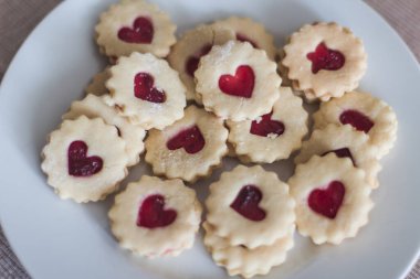 Kırmızı jöle dolgulu leziz kalp şekilli kurabiyeler beyaz bir tabağa konur. Düğün ya da sevgililer günü için tatlı ve romantik bir ortam yaratır.