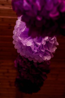 Ahşap bir duvarın önünde asılı mor peçete ponponları bir düğün kutlamasına zerafet ve kapris katarak şenlikli bir atmosfer yaratır.