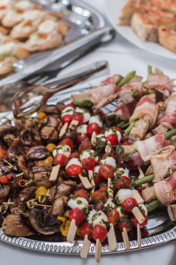 Kiraz domatesleri, mozzarella peyniri ve domuz pastırması paketlenmiş pesto şişleri ve ızgara mantar aperatifleri gümüş tepside, zarif bir gösteri yaratıyor.