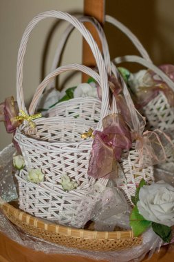 Beyaz hasır sepetler kurdele ve çiçeklerle süslenmiş, düğün hediyeleriyle doldurulmaya hazır, büyüleyici ve şenlikli bir atmosfer yaratıyor.