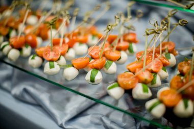 Mozzarella peynirli toplar, fesleğen yaprakları ve kiraz domateslerinden oluşan küçük atıştırmalıklar bir düğün partisinde misafirleri bekliyor, zarif ve iştah açıcı bir gösteri hazırlıyorlar.