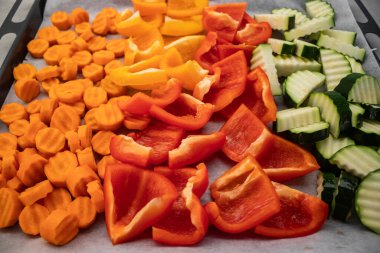 Renkli dilimlenmiş havuç, kırmızı biber, sarı biber ve kabak pişirme tepsisine dizilmiş, kızarmaya hazır, canlı ve sağlıklı bir yemek yaratıyor. Yüksek kalite fotoğraf